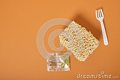 White disposable plastic fork, three block of dry instant noodles and spices on a brown background Stock Photo