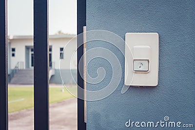 White doorbell or buzzer button on concrete wall beside doorway with house in the background. Stock Photo