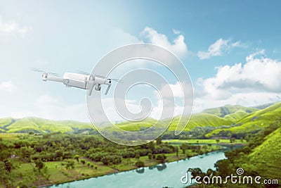 White drone with camera flying over green hills with river and trees Stock Photo