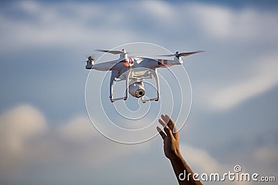 White drone hovering in a bright blue sky with hand ready to cat Editorial Stock Photo