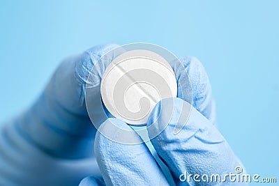 White effervescent or carbon tablet in hand in disposal glove. Doctor, pharmacist or scientist fingers holding pill Stock Photo