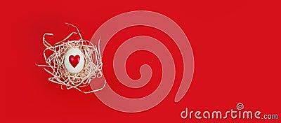 White egg with heart shape in decorative nest on red background with copy space Stock Photo