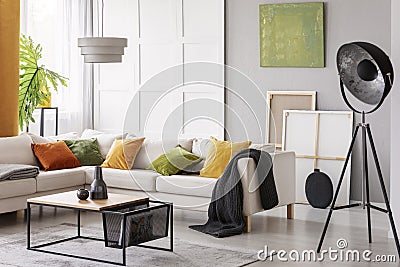 White elegant corner sofa with orange green and yellow pillows in stylish living room interior with modern coffee table and indust Stock Photo