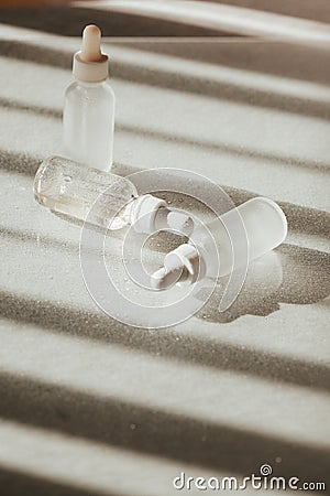 White face serum and face oil bottles with droppers on white reflective tavle with water drops and light and shadow Stock Photo