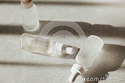 White face serum and face oil bottles with droppers on white reflective tavle with water drops and light and shadow Stock Photo