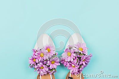 White flat female shoes filled with pink daisies and wildflowers on pastel blue background Stock Photo