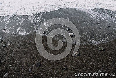 White foam waves wash over the dark lumpy beach Stock Photo