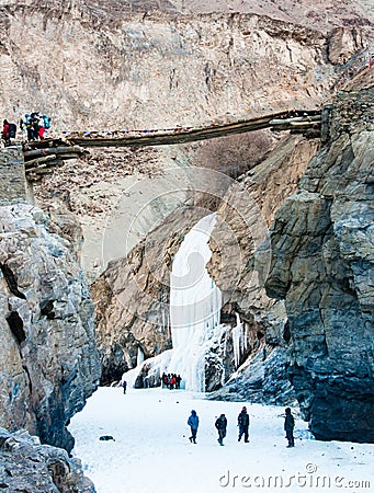 White Frozen waterfall between Mountains. People trekking. Wooden bridge. Zanskar River. Leh Ladakh. India Editorial Stock Photo