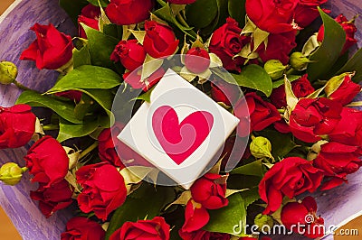 White gift box with red heart on the background of bouquet of red roses in purple wrapping paper. Valentine. Stock Photo