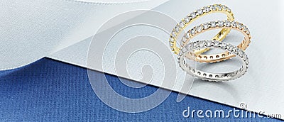 White Gold, Yellow Gold and Rose Gold Eternity Rings Over Background in Blue and White Stock Photo