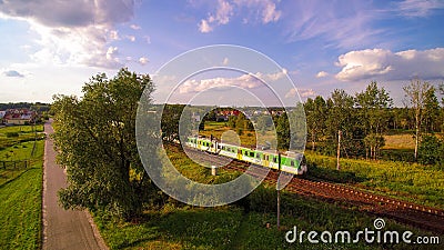White and green train passing through small village during sunny evening. Editorial Stock Photo