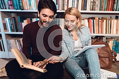 White guy and girl near bookshelf in library. Students are reading books. Stock Photo