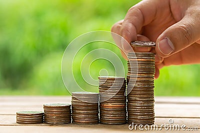 White hand man holding coin to putting on coin stack on table with nuture green bokeh background. Saving money concept or Business Stock Photo