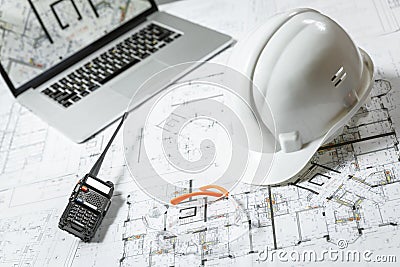 White hard hat, laptop with drawings, glasses and walkie talkie with and blueprints on a table Stock Photo