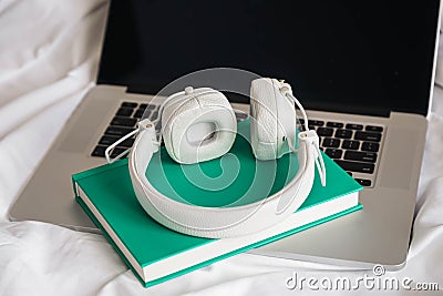 White headphones, green book and laptop in a white bed. Stock Photo