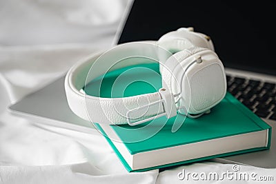 White headphones, green book and laptop in a white bed. Stock Photo