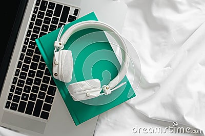 White headphones, green book and laptop in a white bed. Stock Photo