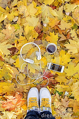 White headphones with a player and a cup of tea and coffee on a background of yellow leaves. Stock Photo