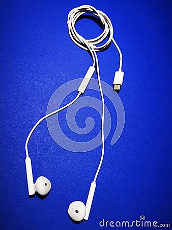 White headphones for a smartphone or an MP3 player with loud and quiet switch on blue background Stock Photo