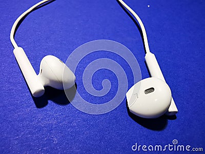 White headphones for a smartphone or an MP3 player with loud and quiet switch on blue background Stock Photo