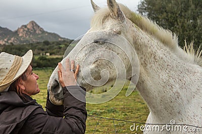 White horse in the green meadow receiving cuddles from his cowgirl with the white cowboy hat with many hugs and caresses and kisse Stock Photo