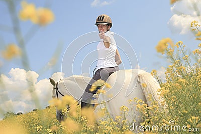 A white horse on yellow flower field with a rider Stock Photo