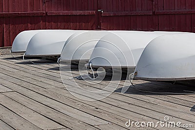 White hulls of small sailboats upside down on a wooden dock, red boathouse background Stock Photo