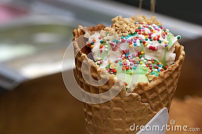 white ice cream in waffle cone with colored sprinkles and falling pieces of nuts Stock Photo