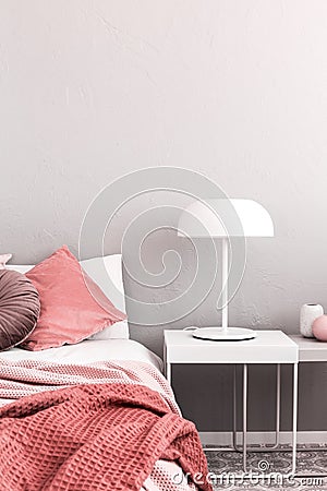 White industrial lamp on nightstand table next to king size bed with white bedding and pastel pink pillows and blanket Stock Photo