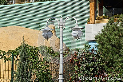 White iron pillar with two lanterns on a street against a wall Stock Photo