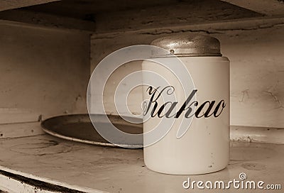 A white jar for storage cocoa with text `Kakao` in russian languige and an old metal tray with rust. Old white kitchen shelf. Sep Stock Photo