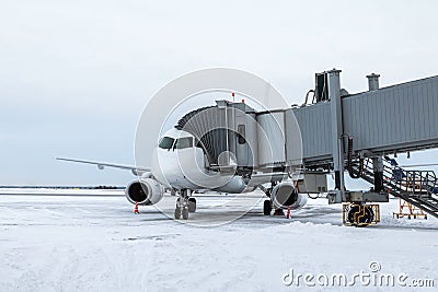 White jetliner at the boarding bridge at winter airport apron Stock Photo