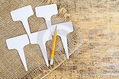 White labels-markers for plants lie on burlap, on wooden background. Stock Photo