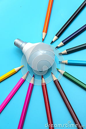 A white LED lamp surrounded by colored pencils on a blue background. The concept of one idea with a difference of opinion Stock Photo