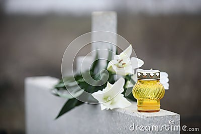 White lilies and candle on light grey granite tombstone outdoors. Funeral ceremony Stock Photo