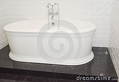 A white luxurious buthtub on a black raised marble platform with a bathtub faucet and shower Stock Photo