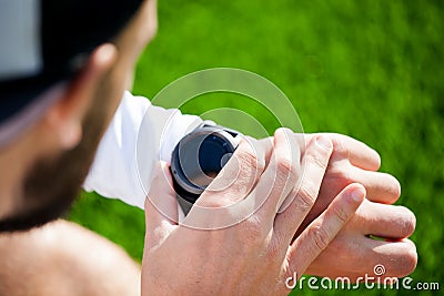 A white man in black shorts and a white shirt looks at a sports watch and adjusts it Stock Photo