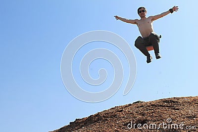 A white man in sunglasses with a bare torso jumped from a hill and flies outstretched arms against a blue sky. The spirit of Stock Photo