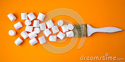 White marshmallows on yellow background with painting brush. Creative concept of unheathy junk food Stock Photo