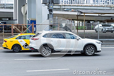 White Mazda CX-9 in motion blur on the street, side view. Japanese big crossover Mazda CX9 riding on the road with industrial Editorial Stock Photo