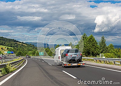 White minibus with tow truck transporter on highway. Car carrier trailer with used car. Beautiful landscape background Editorial Stock Photo