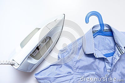 White modern electrical iron close up and blue shirts on the table, top view - ironing, laundry and housework concept Stock Photo