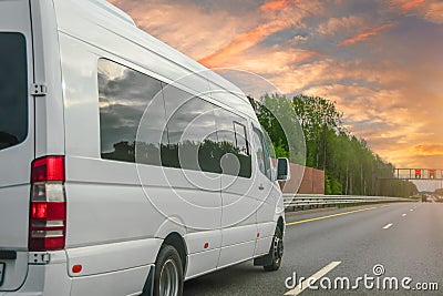 White modern passenger charter van with a small delivery moves fast on the highway to the urban suburbs. Business distribution and Stock Photo