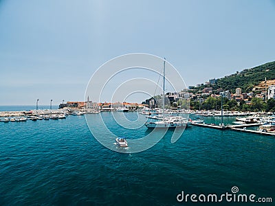 White motor boat sails past the pier of the city of Budva Montenegro on the background of ancient buildings Stock Photo