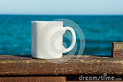 White mug, mock up, empty space for artwork, text, standing on wood plank, turquoise sea, clear blue sky Stock Photo