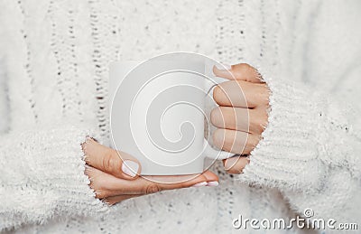 White mug mockup. Girl is holding white 11 oz ceramic cup in hands, wears cozy knitted sweater. Front view, copy space Stock Photo