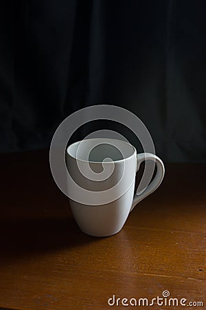 White mug on wooden table with dark blue curtain in background, feel relaxing, best for mockup Stock Photo