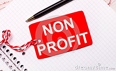 On a white notebook there is a black pen and a red price tag on a string with the text NON PROFIT Stock Photo