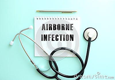 White notepad with the words AIRBORNE INFECTION and a stethoscope on a blue background. Stock Photo