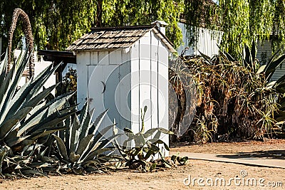 White Outhouse with Cactus Plants in Garden Stock Photo